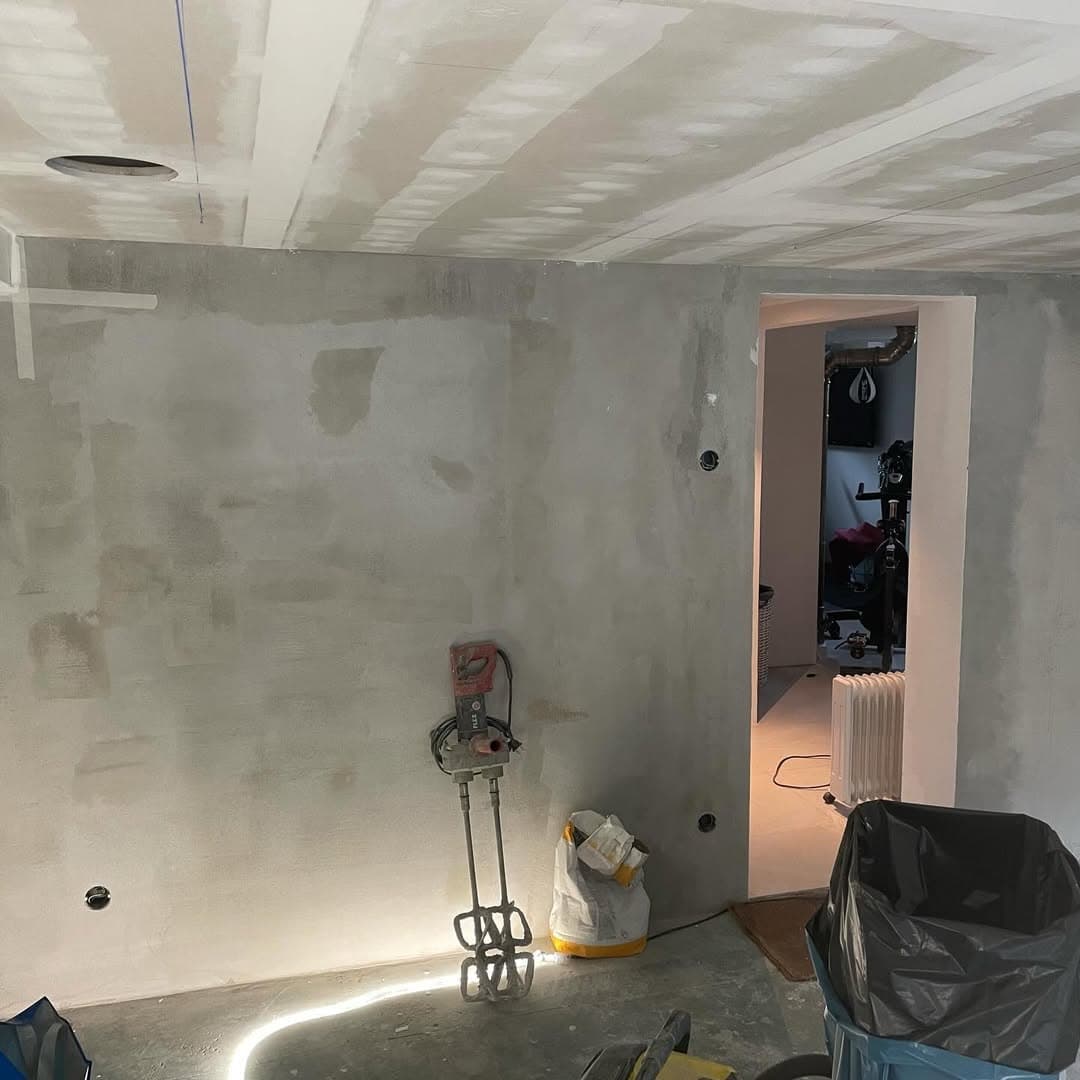Hemmabion innan målning — rå betongvägg och spacklat tak, byggdamm på golvet